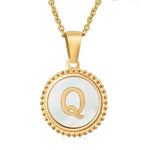 Hanger met vergulde ketting met de letter ’Q’ op een witte ronde achtergrond met kralenrand.