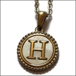 Een hanger van goud en zilver met de letter h