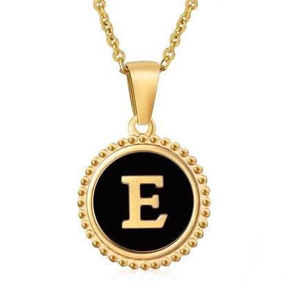 Hanger met vergulde ketting met de letter ’E’ op een zwarte achtergrond met een ronde kralenrand.