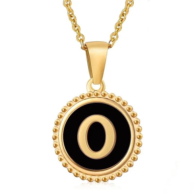 Gouden hangerketting met de letter ’O’ op een zwarte ronde achtergrond met kralenrand.