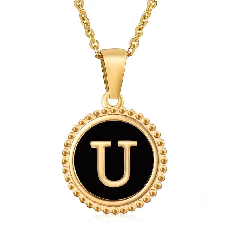 Hanger met vergulde ketting met de letter ’U’ op een zwarte ronde achtergrond met kralenrand.