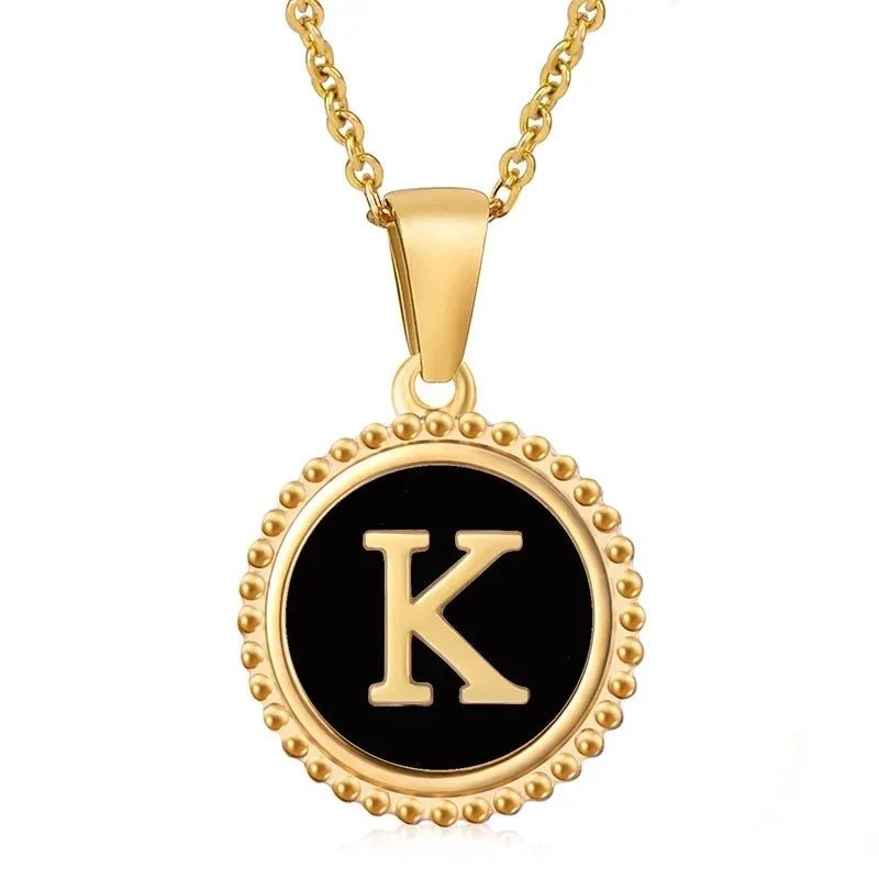 Hanger met vergulde ketting met de letter ’K’ op een zwarte ronde achtergrond met kralenrand.