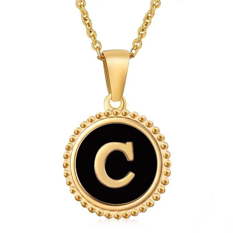 Hanger met vergulde ketting met de letter ’C’ op een zwarte ronde achtergrond met kralenrand.