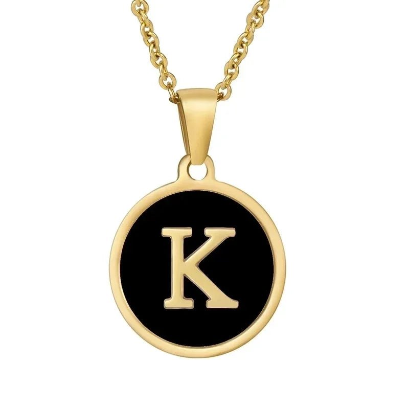 Hanger met vergulde ketting met de letter ’K’ op een zwarte ronde achtergrond.